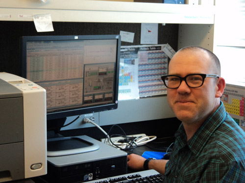 Man with glasses sitting in front of a screen, looking at camera