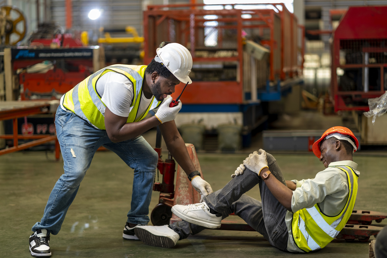 factory worker having accident while working in manufacturing site while his colleague is asking for first aid emergency team using walkie talkie radio for safety workplace usage