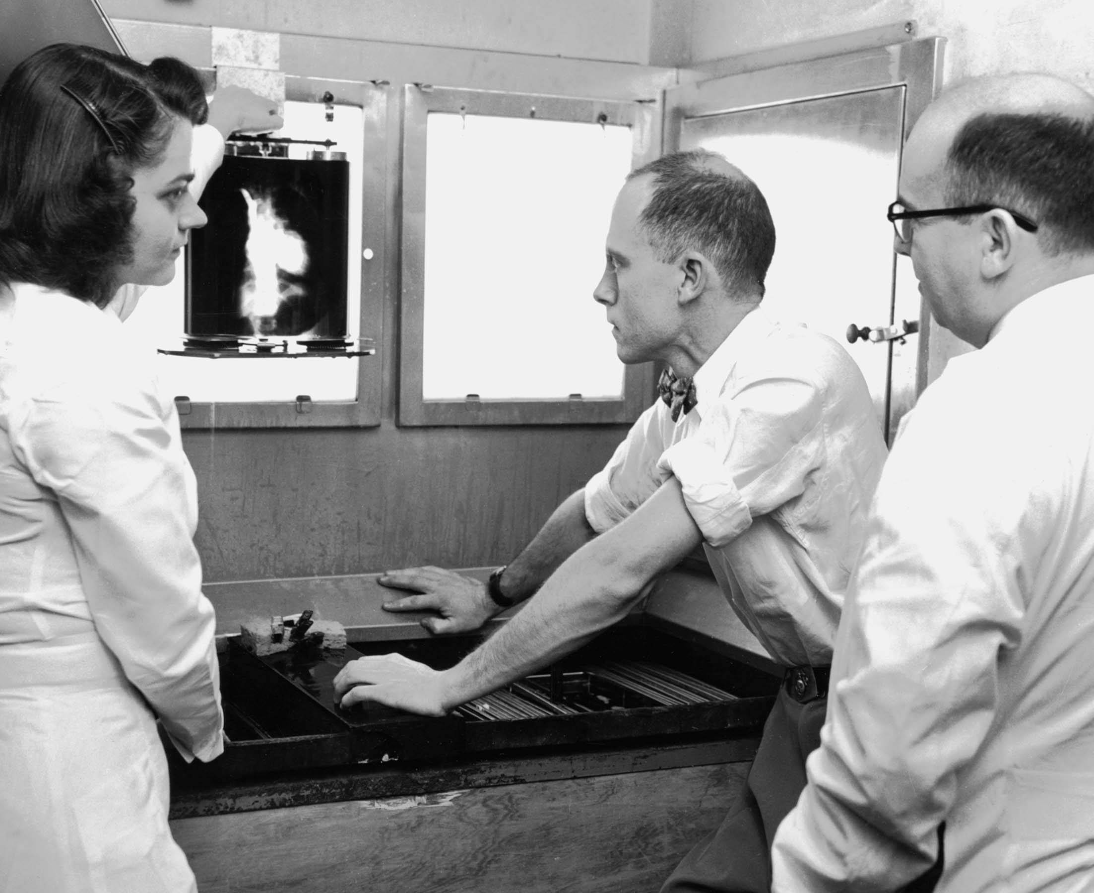 Black and white image of two men and one woman looking at an xray