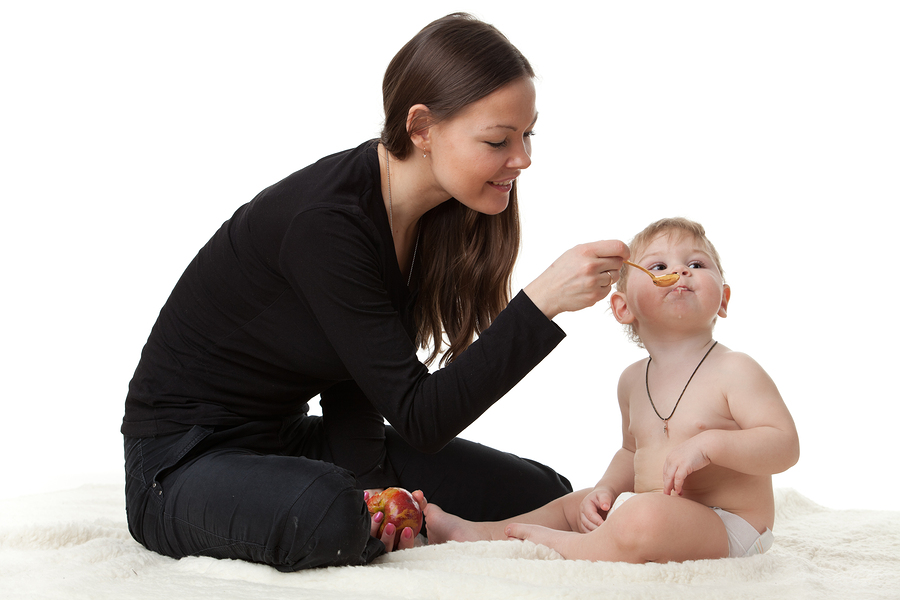 Young woman sitting on the floor, feeding a baby also on the floor