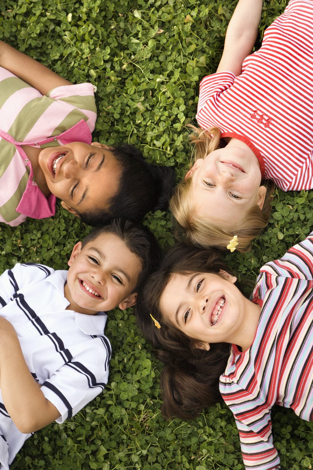 four children lying with heads touching on clover
