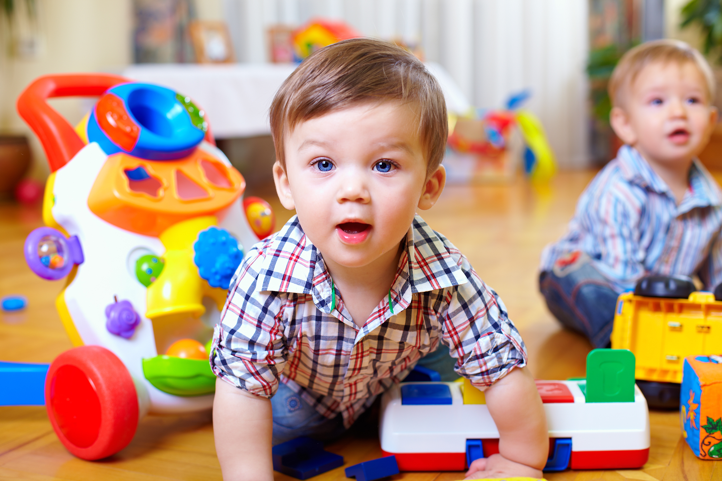 Two infants playing with toys on the floor