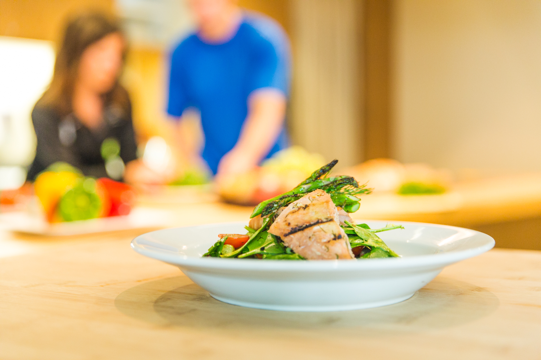 White plate of salmon salad on counter with couple in the background.