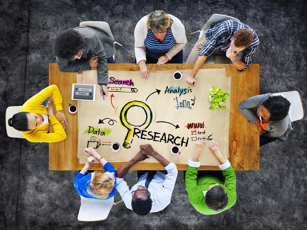 People sitting around a table collaborating with research written in the middle
