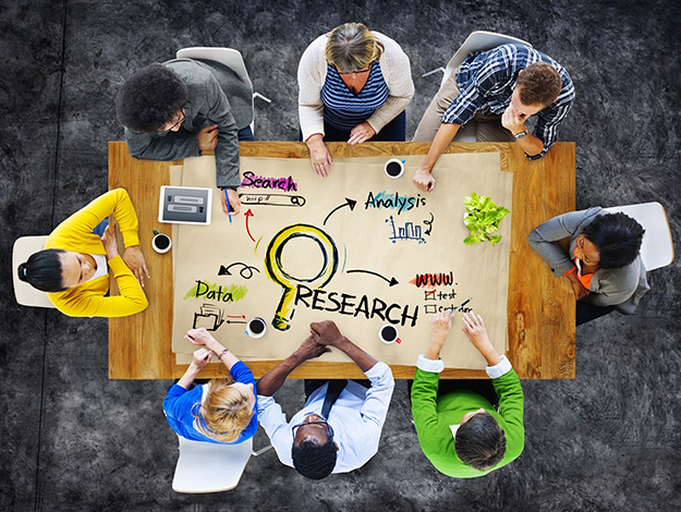 Group of eight people sitting at a table collaborating about research, which is written on the table