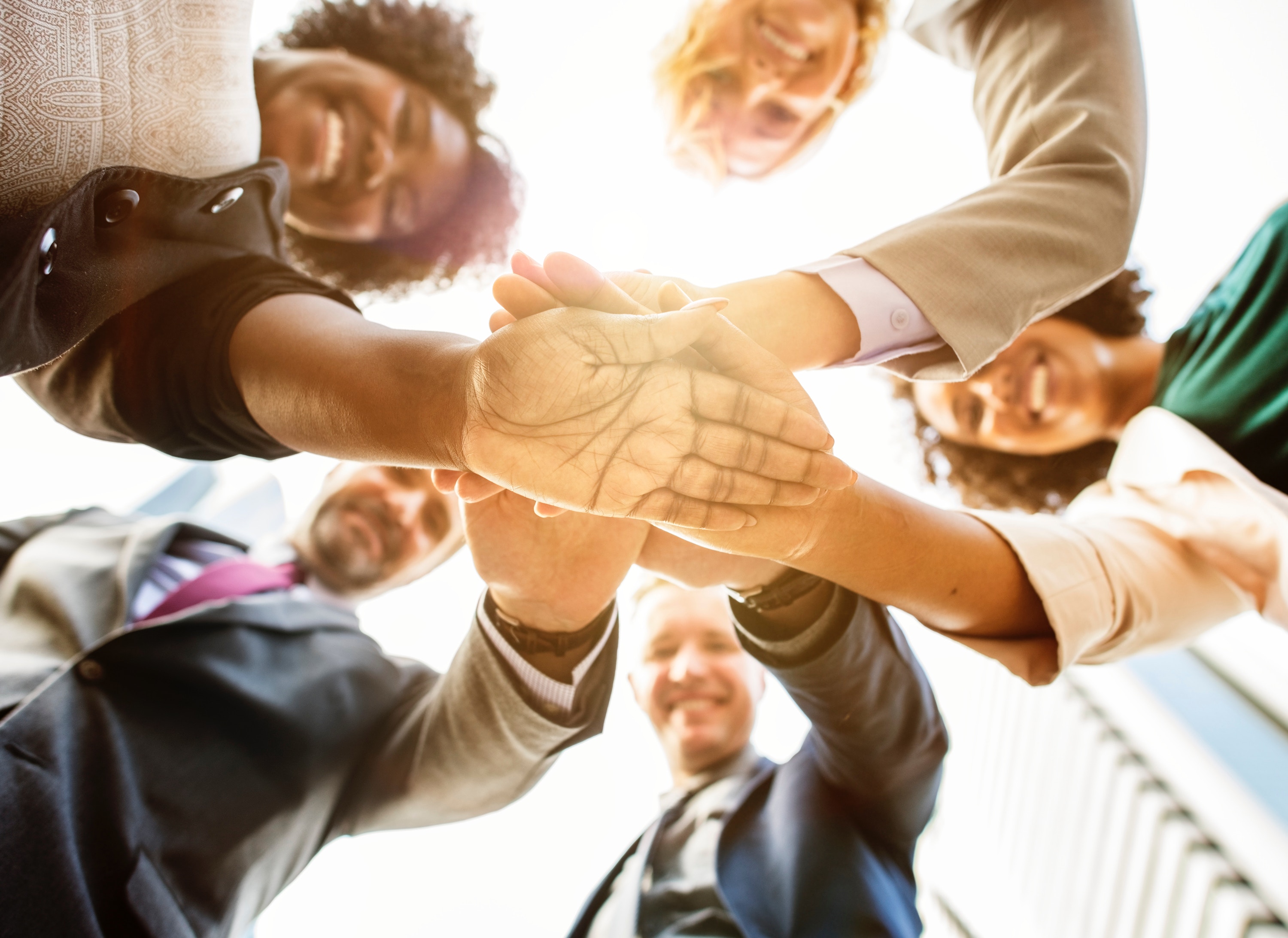 Five people putting/stacking their hands together shot from below them in the sun