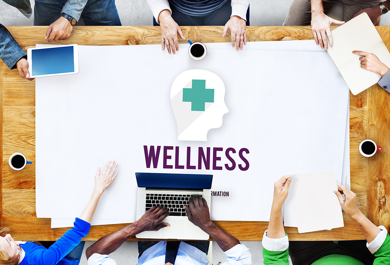 People sitting at a table collaborating with Wellness written on table