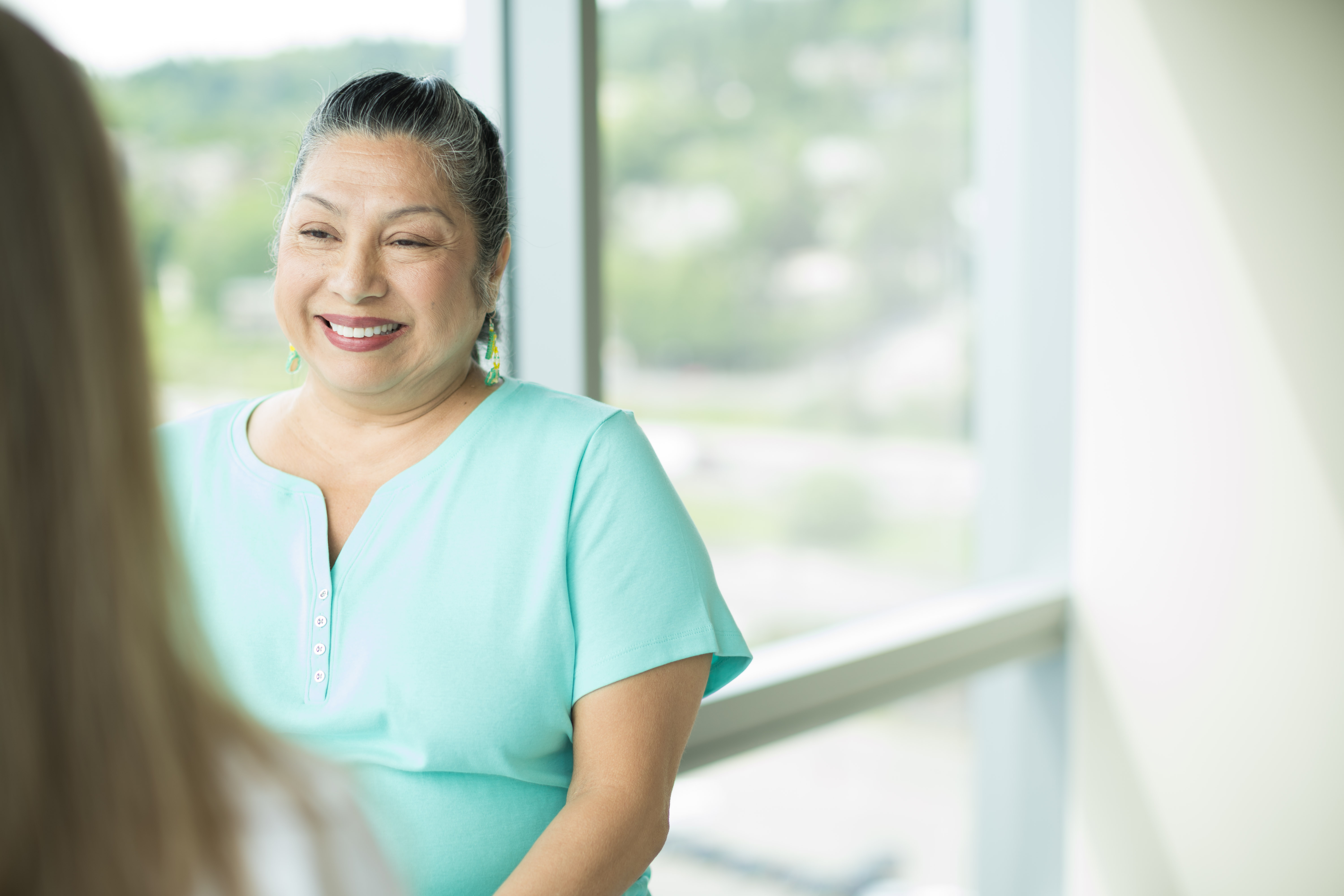 Photograph of a smiling woman in a clinic room with a window. At the 博彩网站 Parkinson Center, patients receive care from a team of experts.