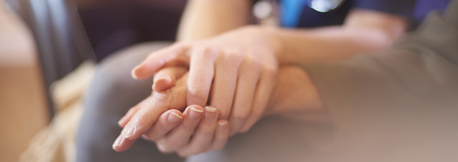 A person clasping their hands around another person's hand in a comforting manner