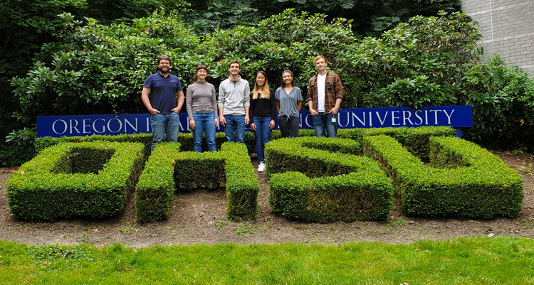 Pruneda Lab researchers stand outside in front of an Oregon Health & Science University sign, behind bushes trimmed to spell, "博彩网站."