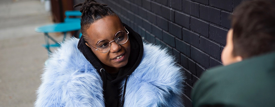 Photo of a person in a fluffy blue coat talking to another person.