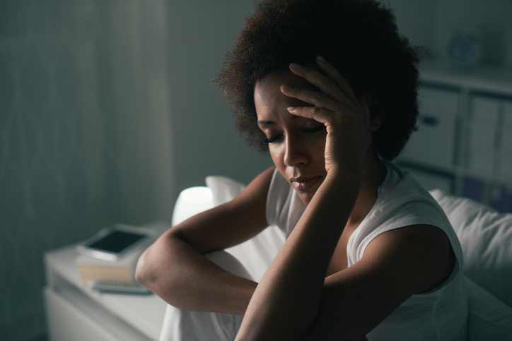Woman holds hand to head in dark room with her eyes closed