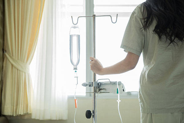 View from behind of woman holding IV pole in front of window