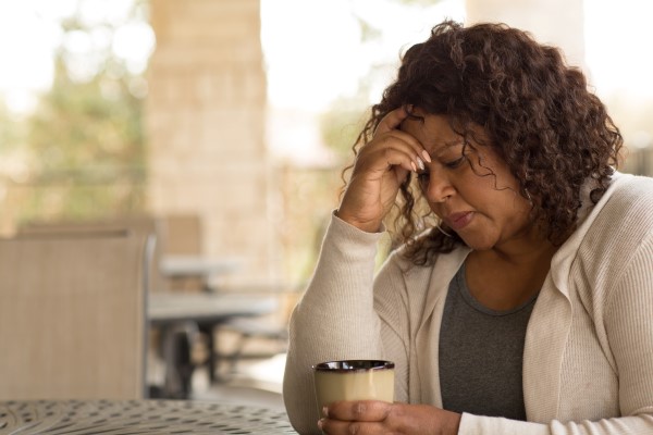 Women touches forehead while holding a mug in her other hand.