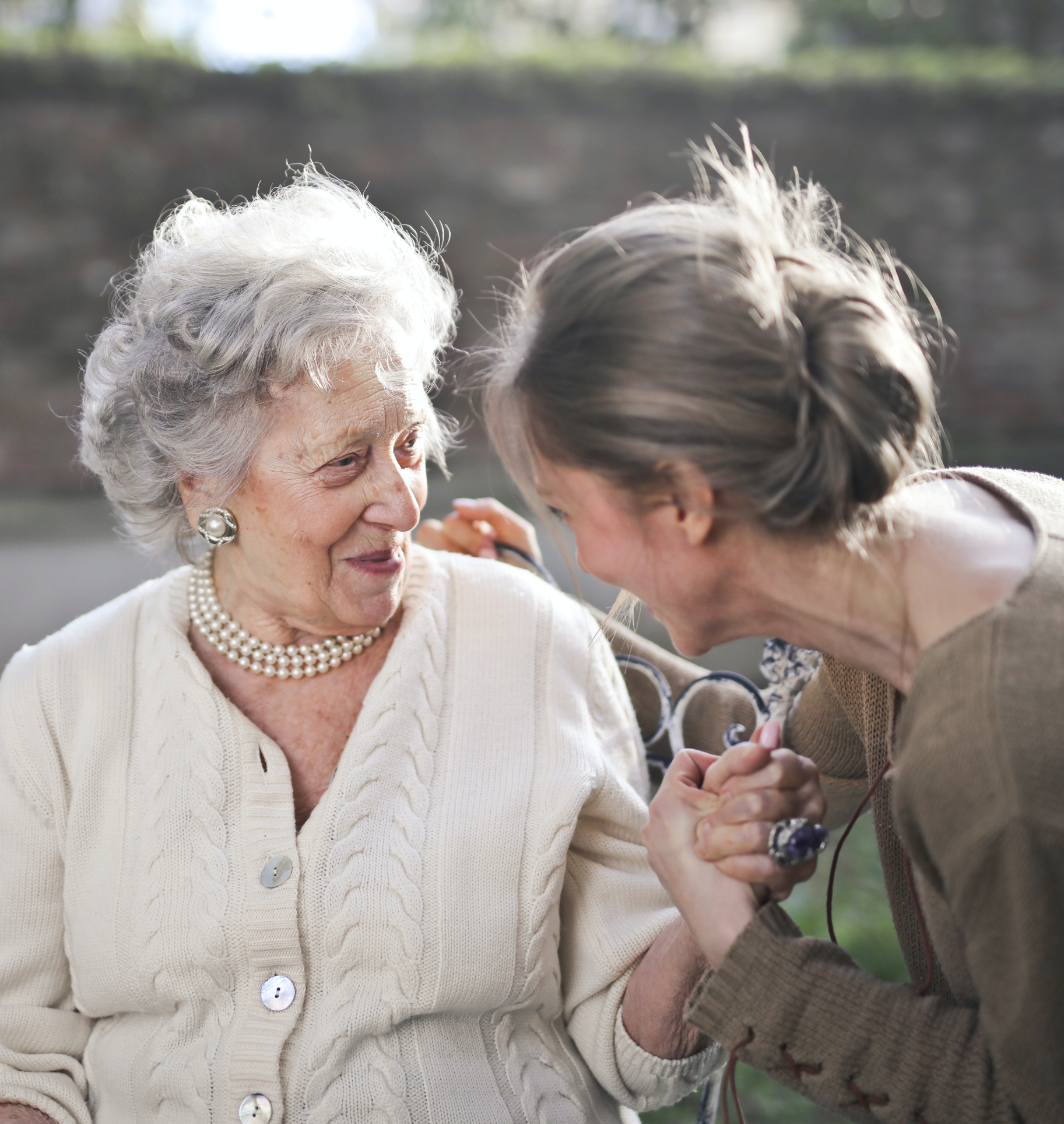 Younger female caregiver talks with older female relative in the backyard