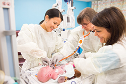 Three female 博彩网站 providers smiling as they care for a newborn baby.
