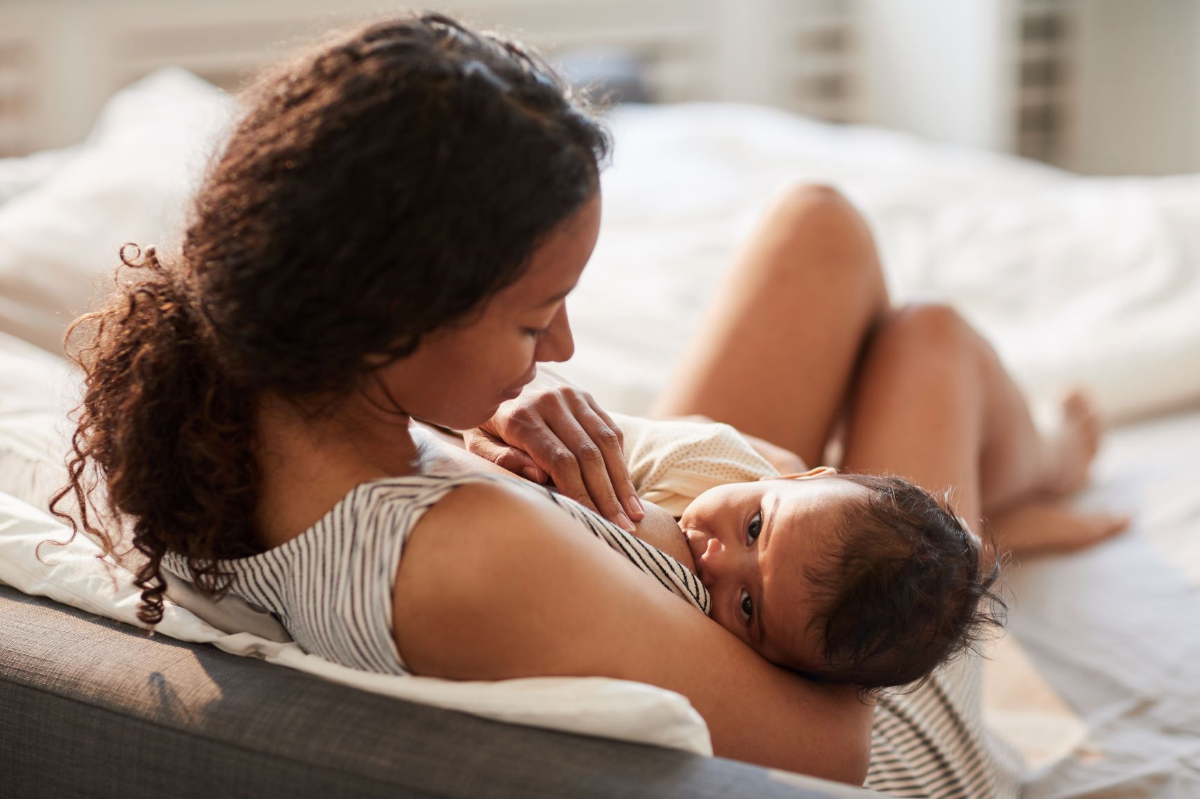 Woman rests on bed and breastfeeds an infant.