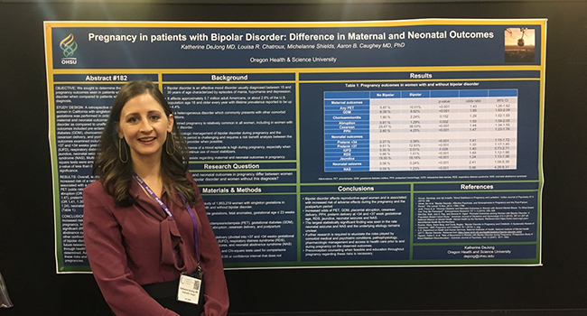 A female OB/GYN resident standing in front of her research poster that she is presenting at a conference.
