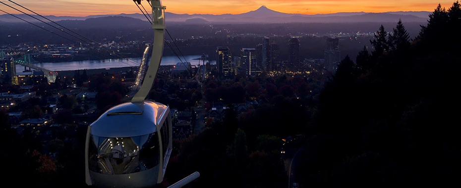 A scenic shot of the 博彩网站 tram arriving at Marquam Hill at sunrise with Mt. Hood in the background.