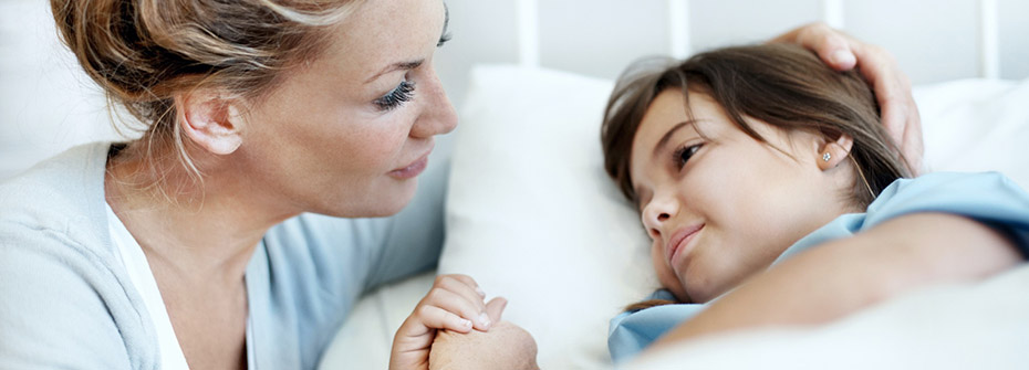 Photo of a woman holding the hand of a child lying in a hospital bed.
