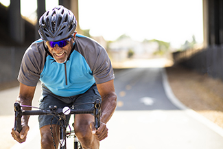 A man smiling while riding his bicycle down the street on a sunny day.