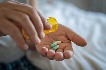 Stock photo of a pair of hands holding a light brown plastic bottle and several green and white capsules