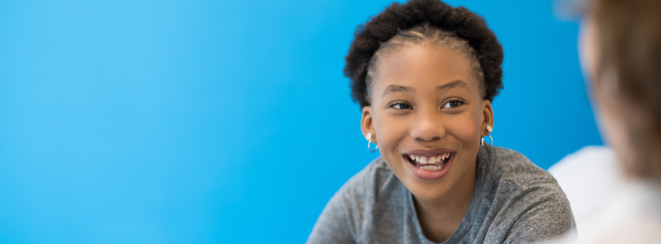 Photo of a child smiling sitting in front of a blue wall.