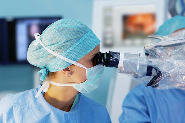Stock photo of a person wearing a surgical cap and face mask looking into a microscope
