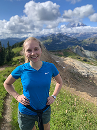 A photo of a woman smiling with her hands on her hips while on a hike.