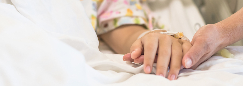 Photo of an adult holding a child's hand - the child being a patient lying in a hospital bed.