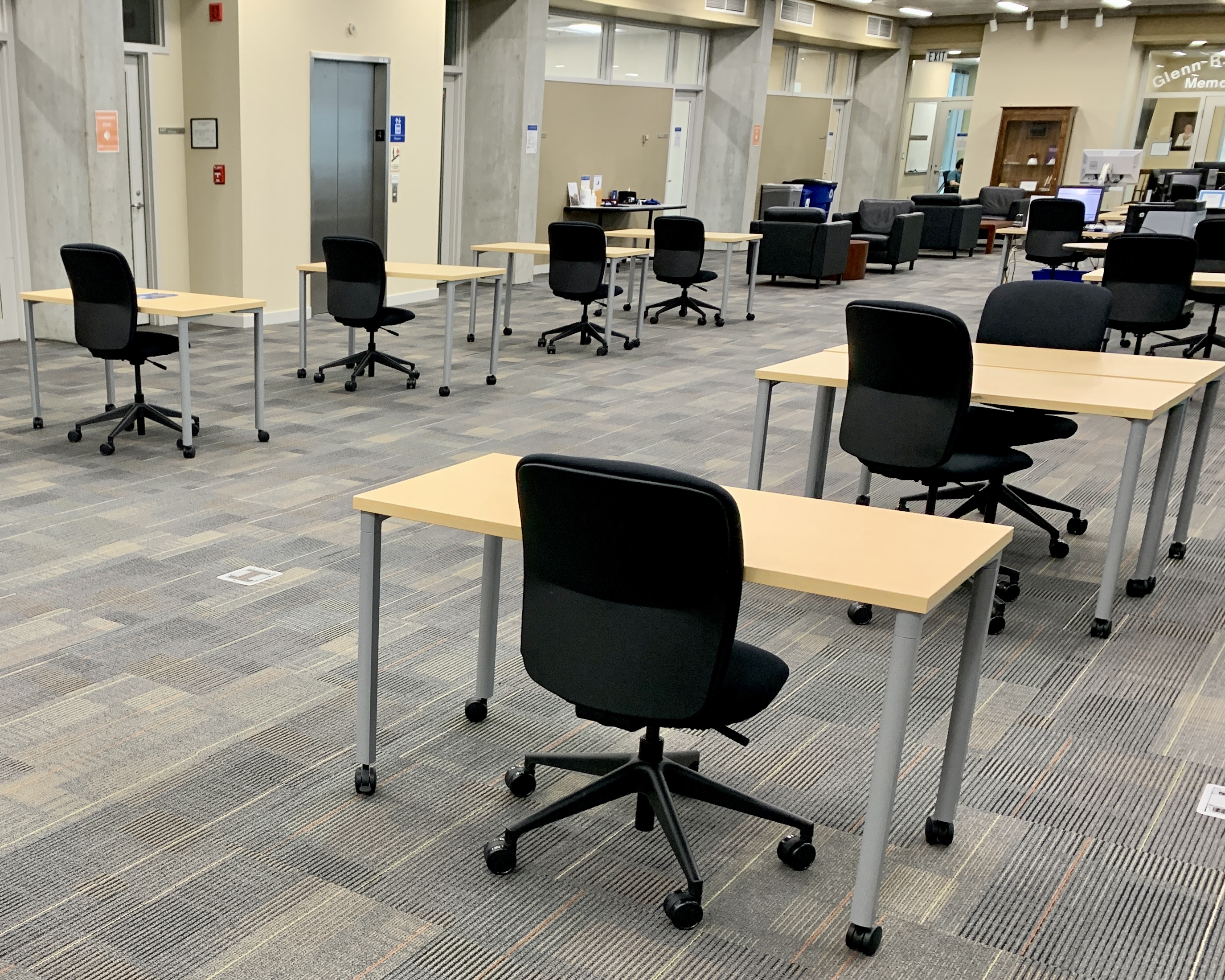 An open library sapce depicts rows of individual desks on wheels with black office chairs on wheels sitting at each.