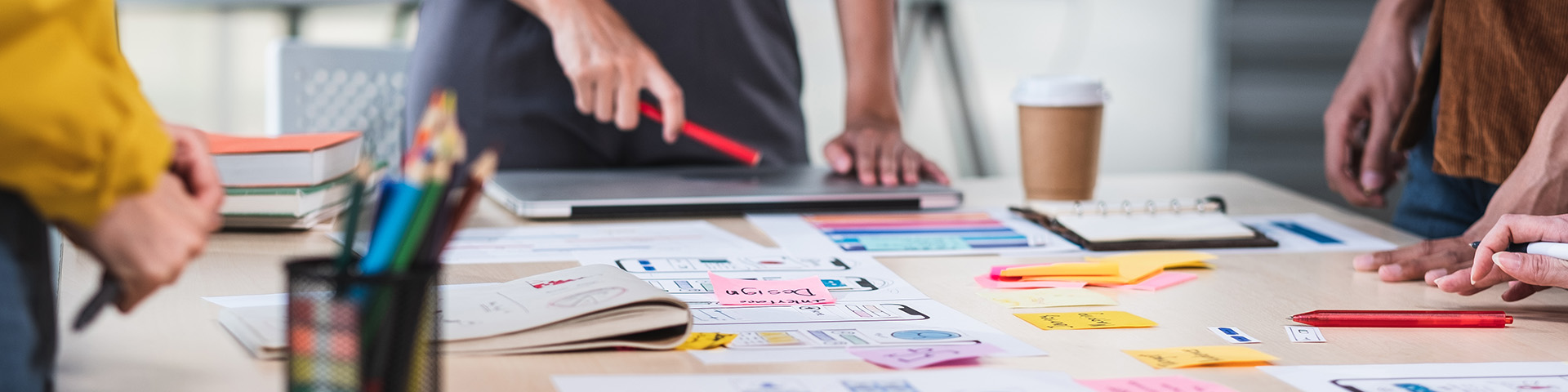 Individuals standing over a desk of papers, computers and sticky notes. Image courtesy of Getty Images