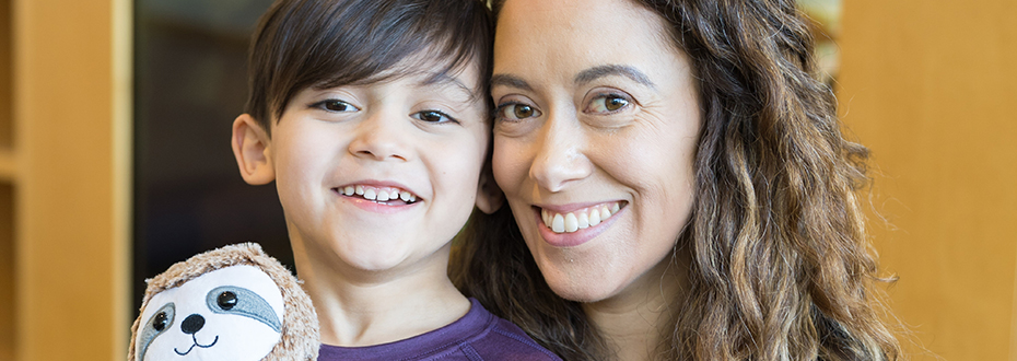 A woman with her arm around a young boy who is holding a stuffed animal.