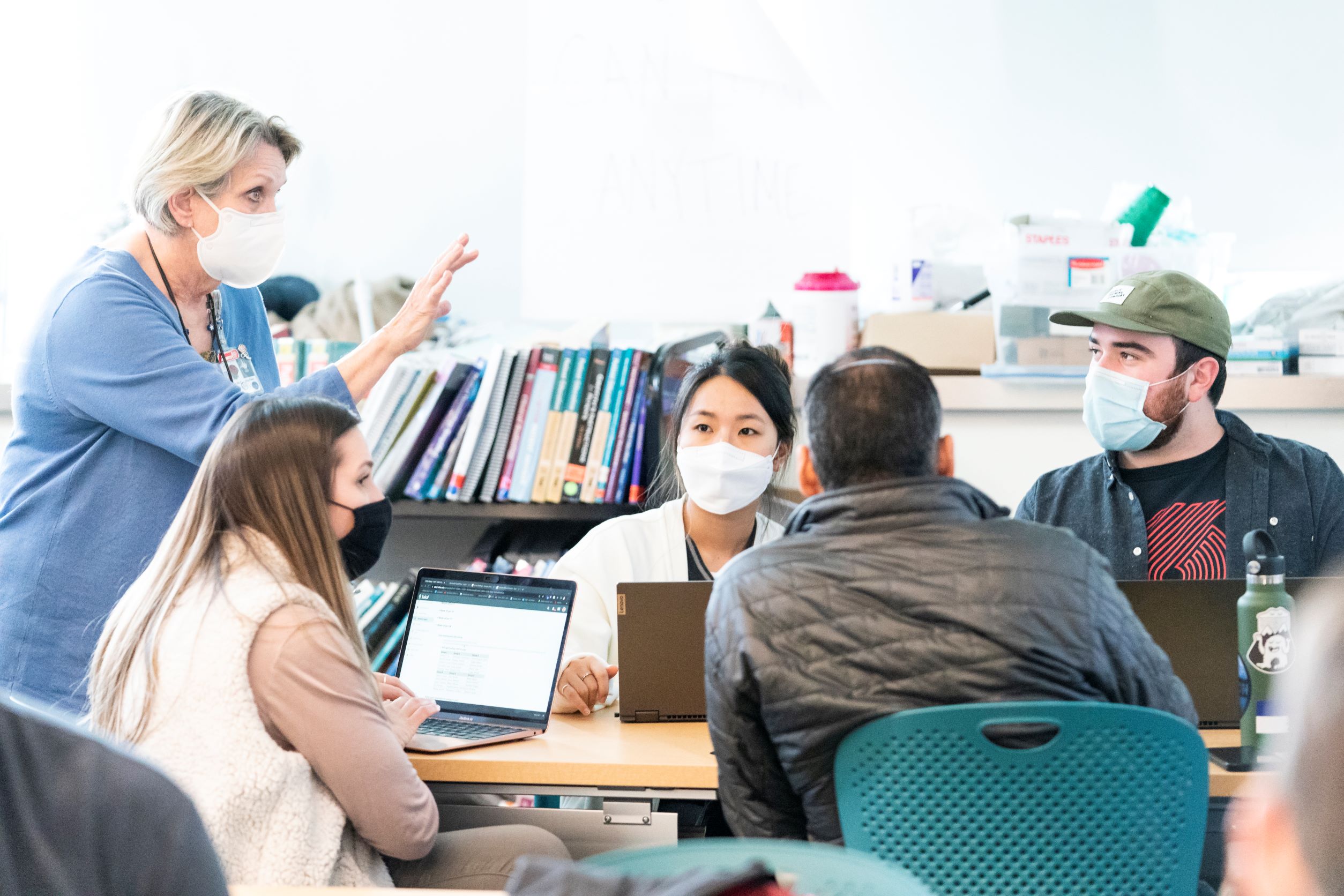 A faculty member is standing at the end of a table speaking to a group of seated students.