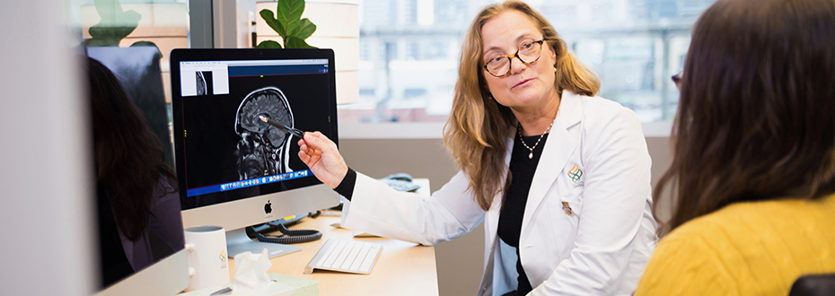 Dr. Jackie Bernard reviewing a computer on desk in a white lab coat