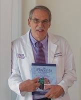 Dr. Myatt is wearing a white lab coat and holding a placenta textbook.