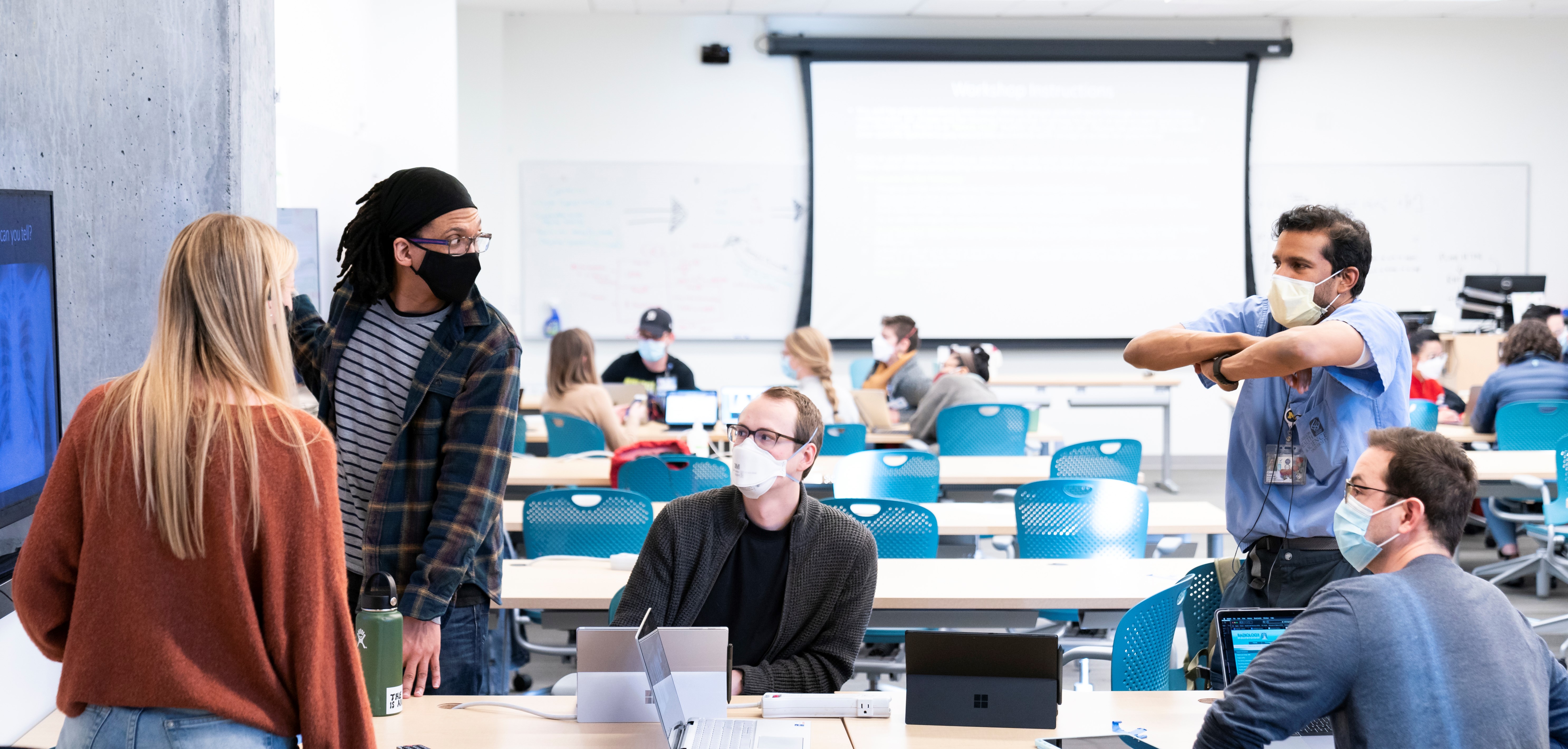 Students sitting and standing around a table discussing with instructor.