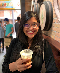 A woman smiling while holding a frothy drink that gave her a froth mustache.