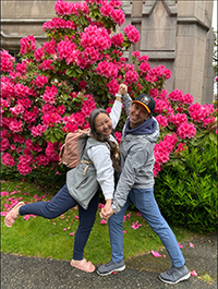 A man and a woman embracing in front of a flower bush.