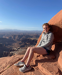 A woman sitting on a rock ledge in the mountains.