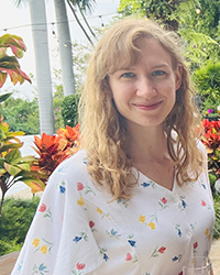 A woman smiling outside with plants behind her.