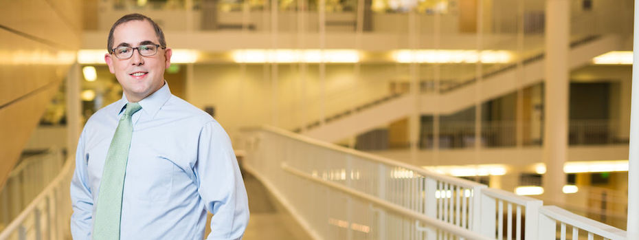 Surgeon Kenneth Gundle stands smiling in a light, airy hospital corridor.