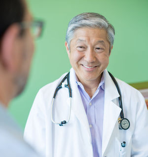A doctor smiles in warmth and reassurance to a patient in a clinic.