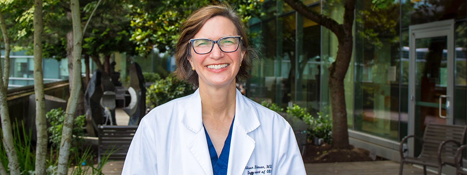 Dr. Alison Edelman stands on a wide balcony outside the 博彩网站 Center for Women’s Health. She wears a white doctor’s coat, and smiles broadly.