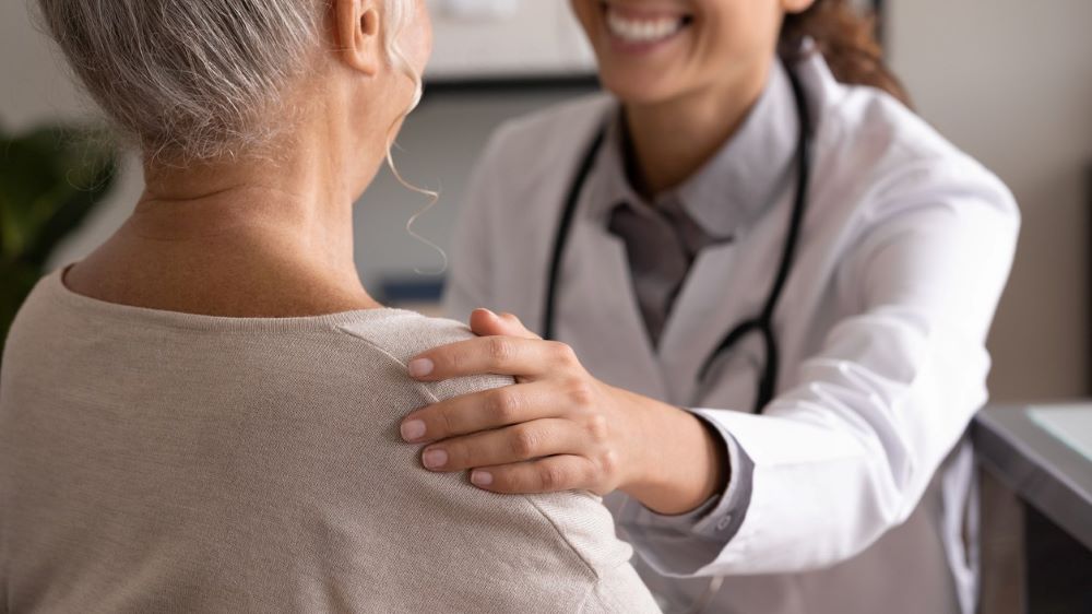A provider places her hand on a patients shoulder, providing comfort, while smiling
