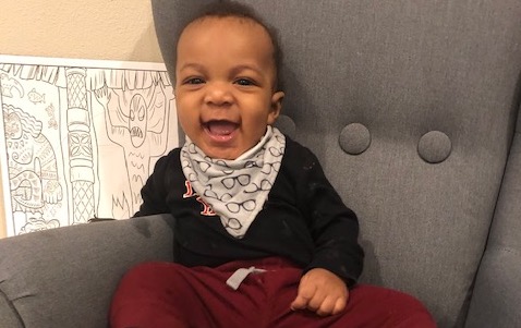 A baby boy sitting in a chair smiling.