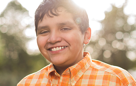 A photo of a young boy outside on a sunny day smiling.