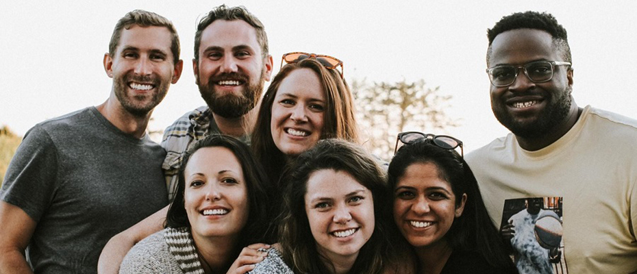 A group photo of three men and four women together smiling outside.