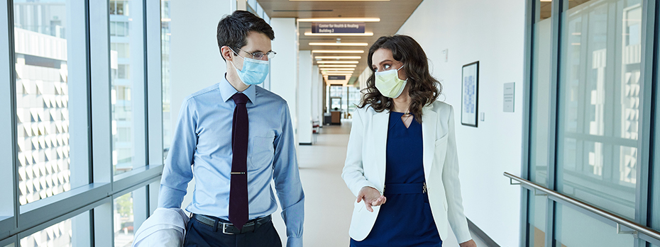 Two doctors, a man and a woman, talk while walking down a hallway at 博彩网站