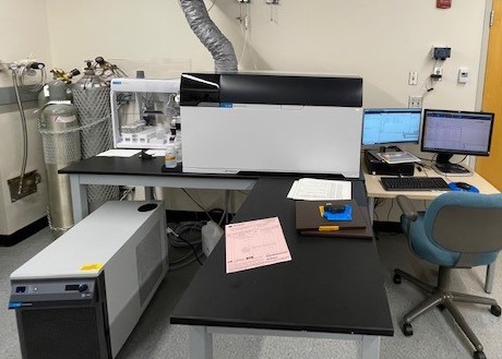 An Agilent 8900 ICP-QQQ sitting on a large desk, between a desktop computer set-up and an Agilent SPS 4 autosampler.